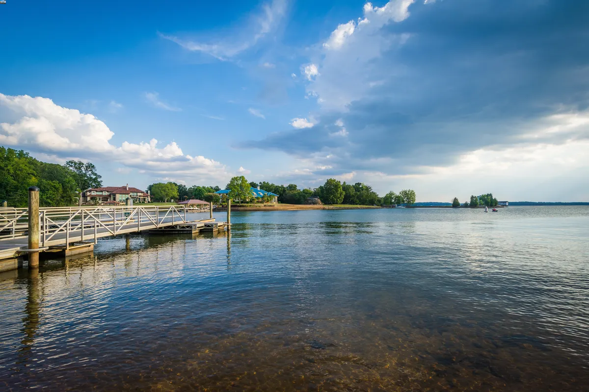 A tranquil scene of a dock on the water, accompanied by a house and flourishing trees in the background.